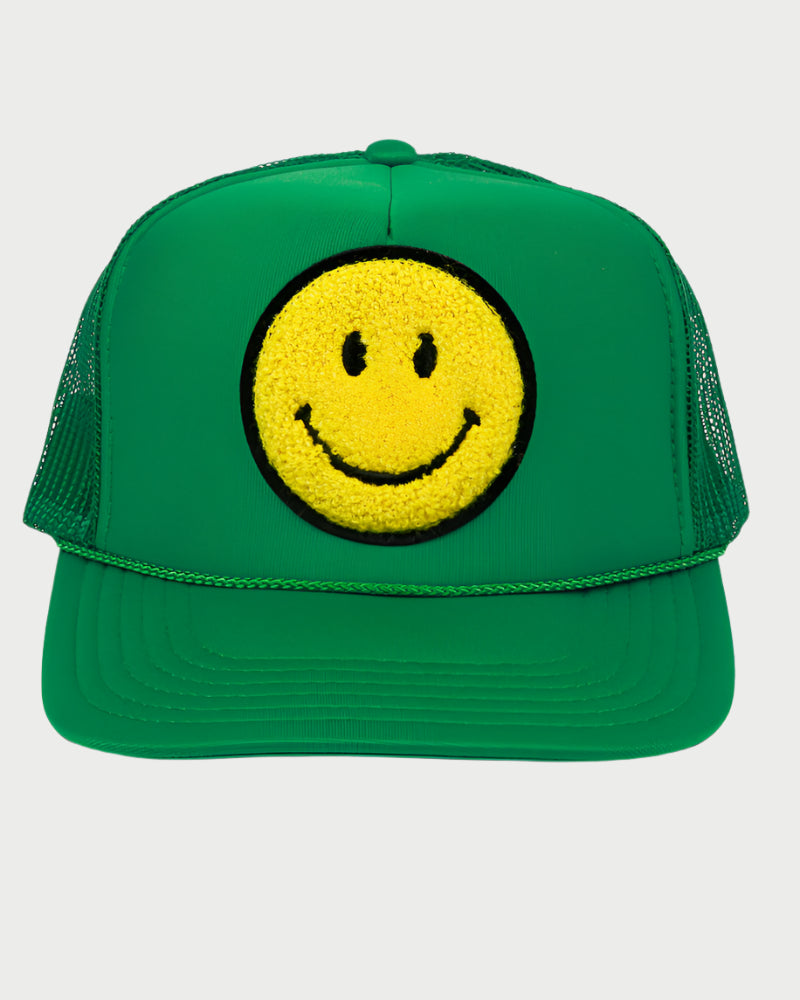 The Smiley Patch Trucker Hat by LOCAL BEACH features a green mesh back and a bold yellow chenille patch smiley face on the front. Its black eyes and mouth stand out against the plain white background, creating a cheerful design.
