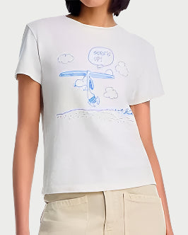 A person wears the RE/DONE Surf's Up Snoopy Tee—made of 100% cotton and featuring a blue cartoon airplane with a "SURF'S UP!" speech bubble—paired with light-colored pants.