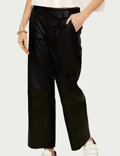 Against a neutral backdrop, an individual dressed in SPRWMN Cropped Baggy Leather Trousers showcases effortlessly chic style. With a hand tucked into a pocket and a gold bracelet adorning the other wrist, their white shoes complete the look alongside part of their cropped silhouette top.