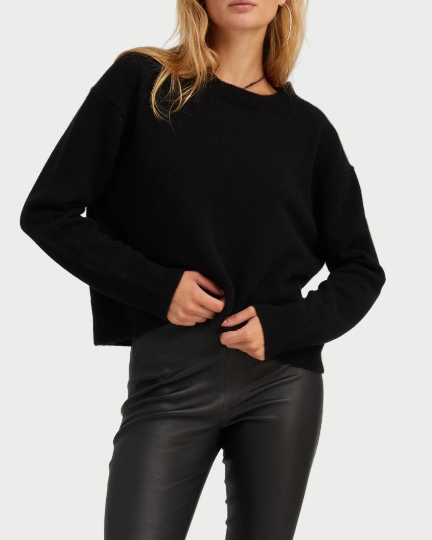 Woman wearing a black sweater and sunglasses on a light gray background