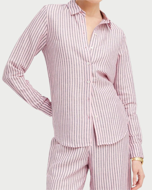 A person wears the SPRWMN Fonda Button Down Stripe Shirt in pink and white stripes, featuring a collared, long-sleeve design with matching pants. The breathable fabric ensures comfort, accessorized with a gold wristwatch.