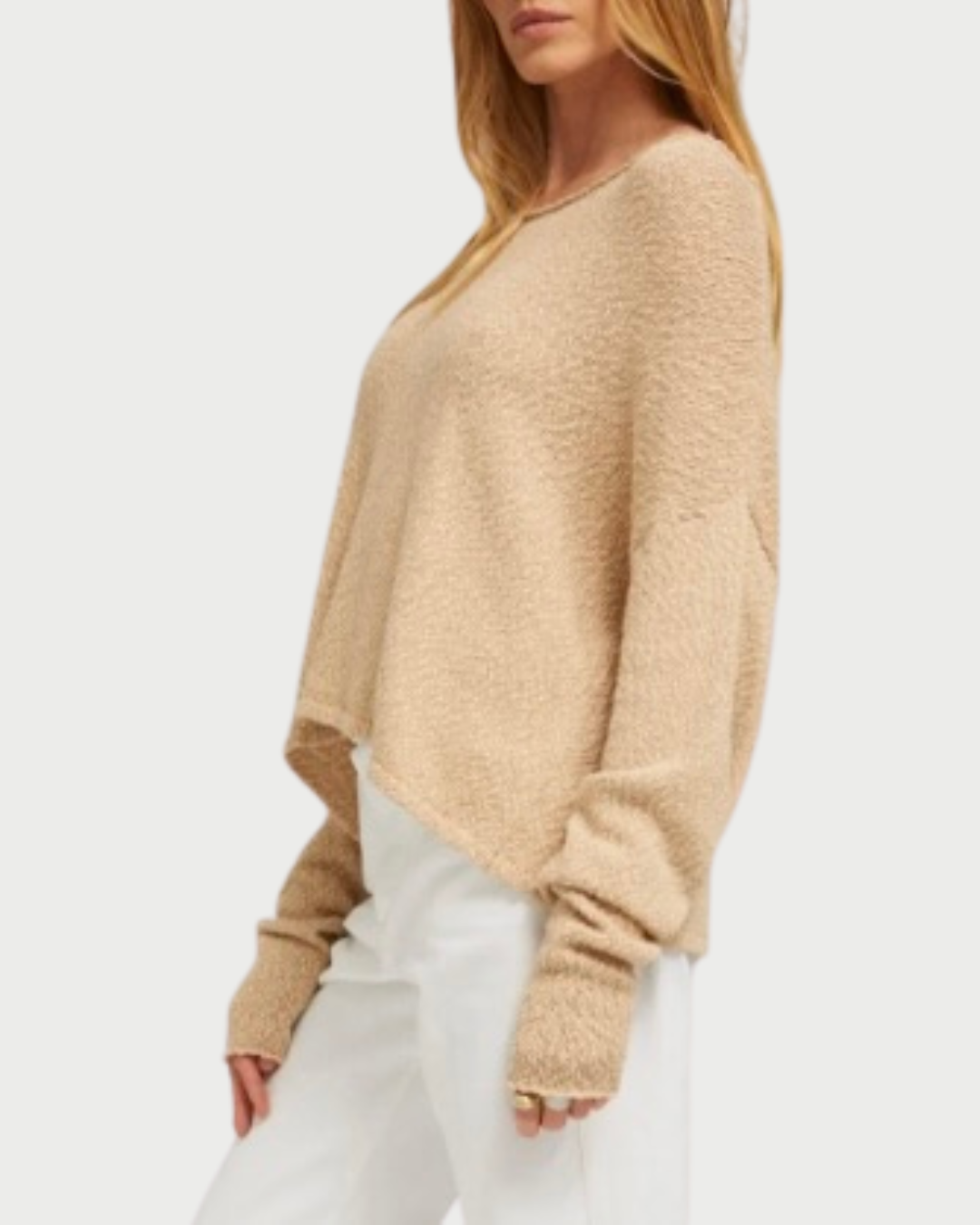 A woman wears the SPRWMN Off Shoulder Sweater—a loose, beige cotton bouclé style with long sleeves by SPRWMN—paired with white pants, standing with one arm relaxed at her side against a plain white background.