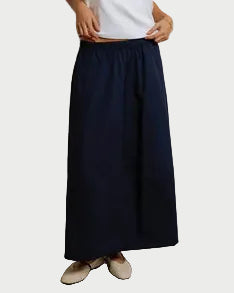 Woman wearing a white top and navy pants against a plain background