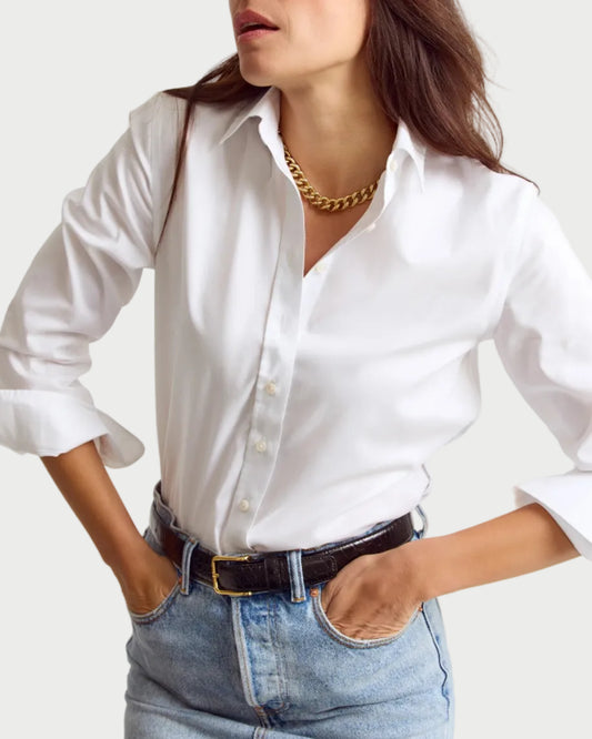 Woman wearing a white shirt and blue jeans with a gold necklace on a plain background