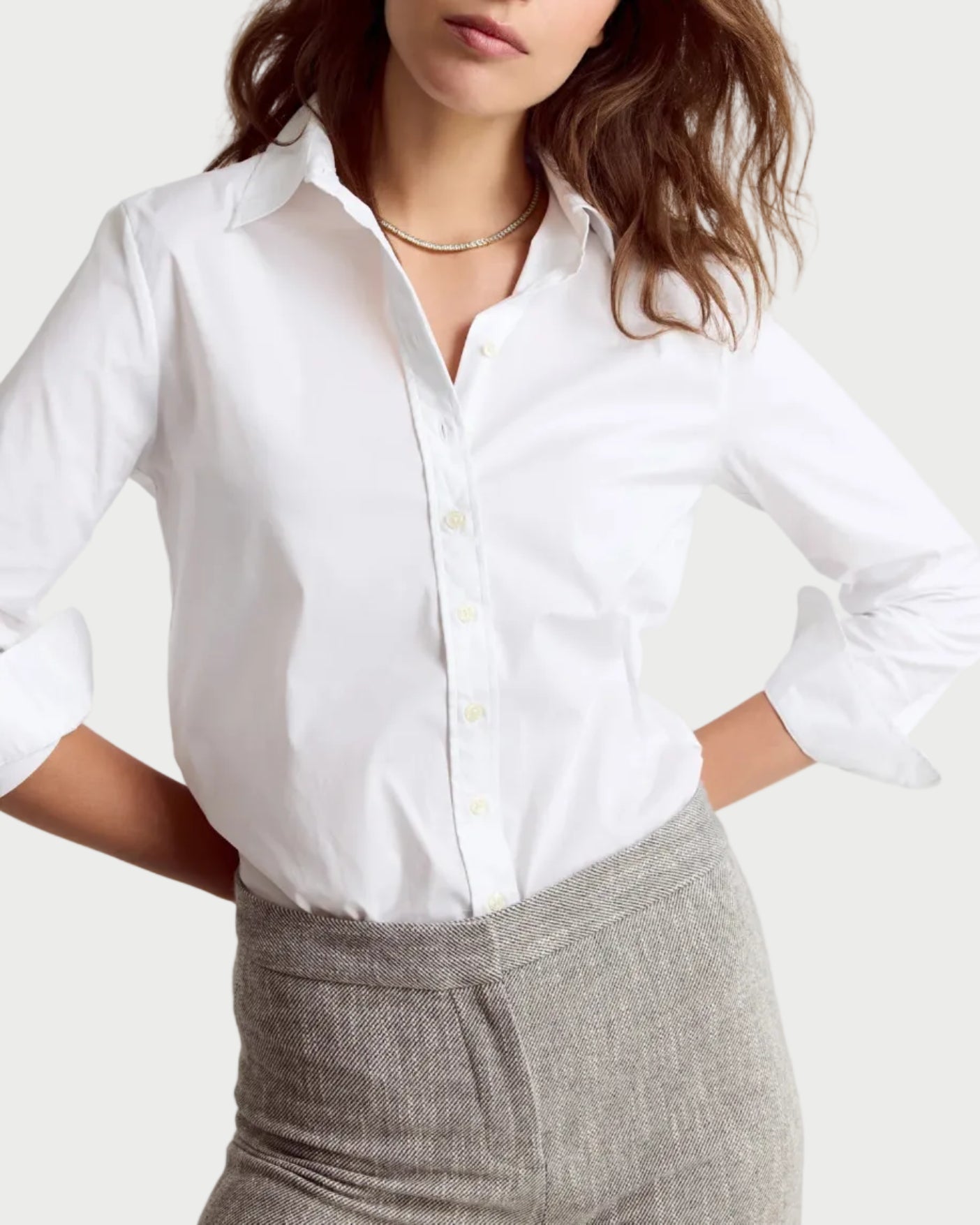 Woman wearing a white shirt and gray pants on a plain background