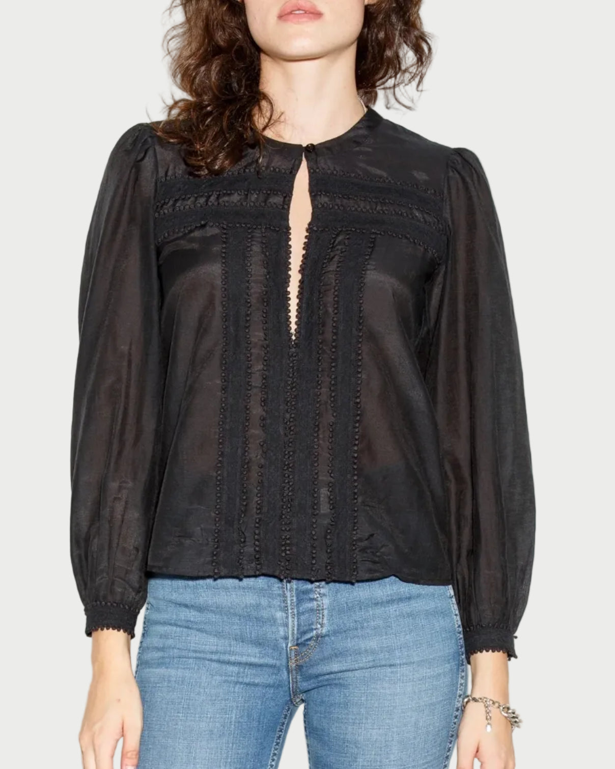Woman wearing a black blouse with sheer details and blue jeans against a white background
