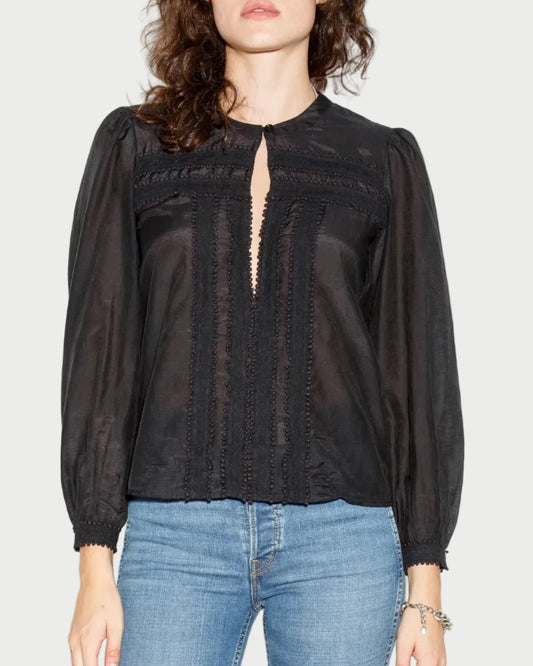 Woman wearing a black blouse with sheer details and blue jeans against a white background