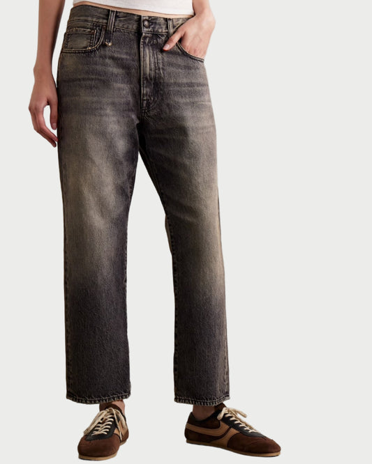 Person wearing dark jeans and brown shoes on a plain background