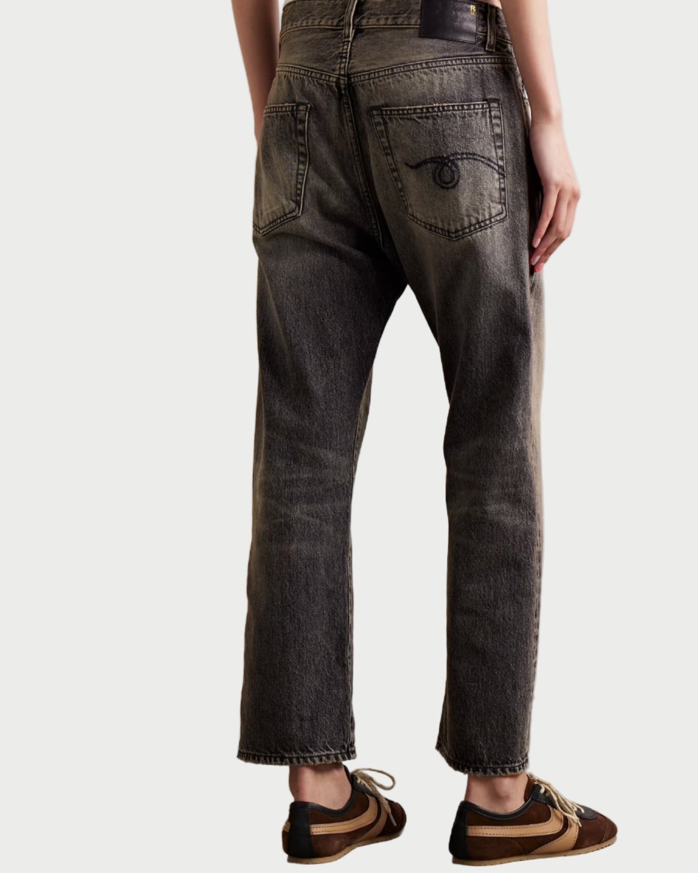 Person wearing dark jeans and brown shoes on a plain background