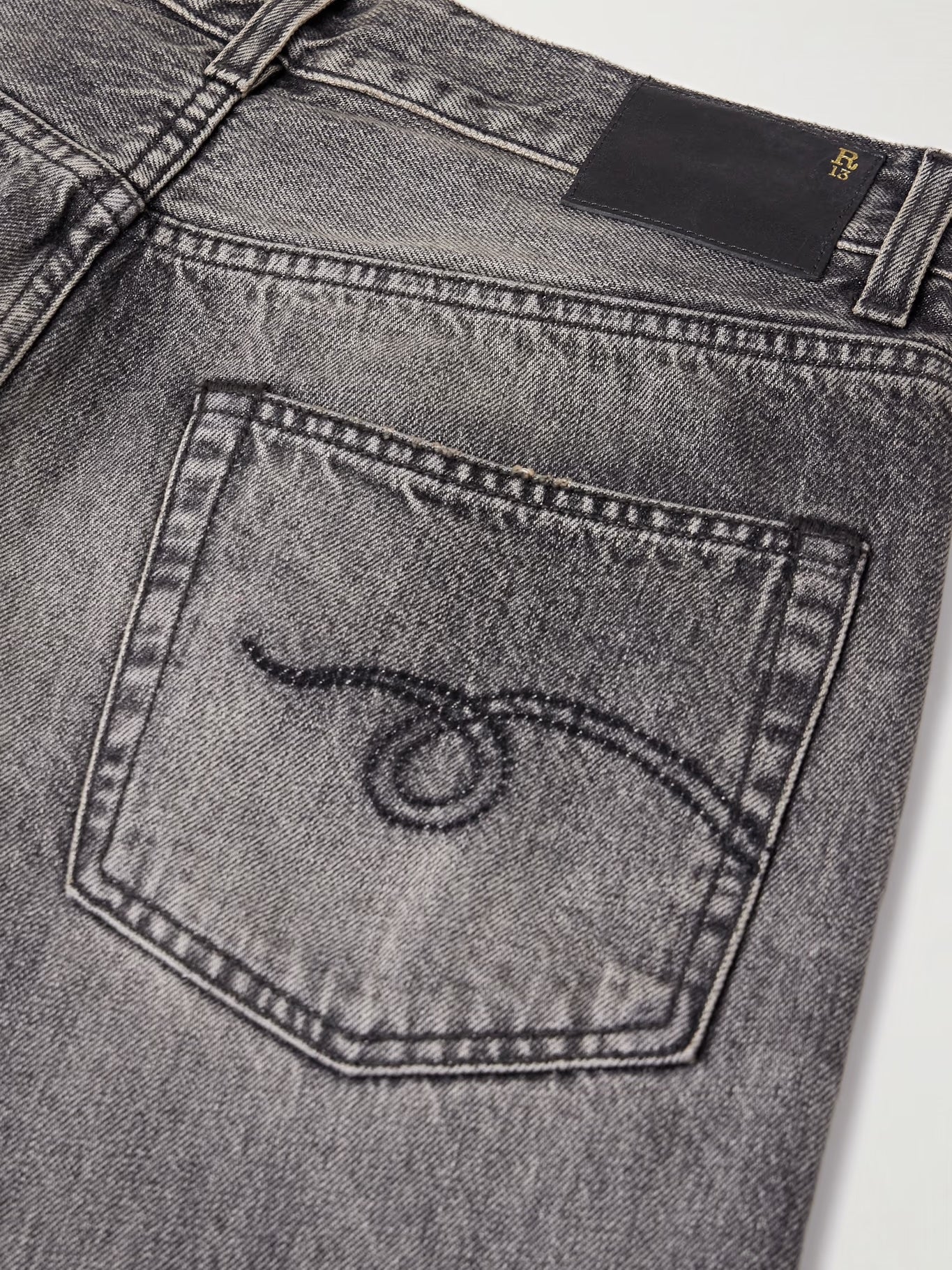 Close-up of the back pocket of R13 Boyfriend Jeans Leyton Black, showing an eye-like stitched design, a black leather waistband patch, and a subtle vintage wash for character.
