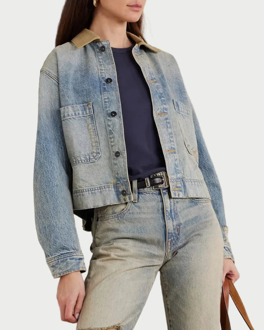 Person wearing a denim jacket and jeans holding a brown handbag indoors.