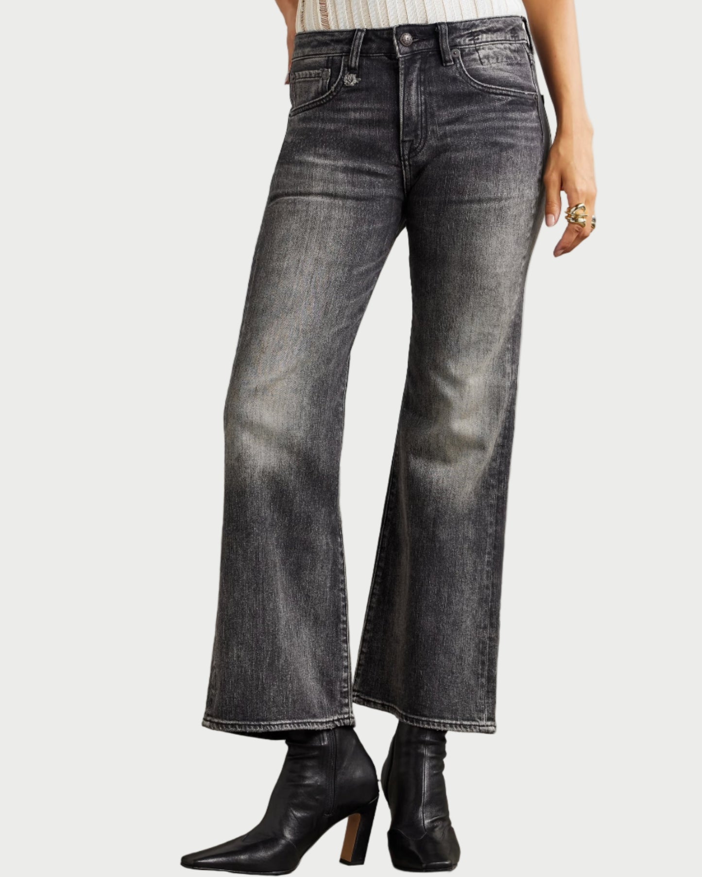 Person wearing black flared jeans and black boots on a neutral background