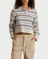 A woman stands against a draped cream fabric backdrop wearing a cropped long-sleeve polo-style top with navy and cream horizontal stripes, paired with loose beige drawstring pants and dark sandals.