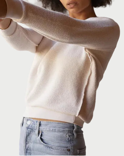 Woman wearing a beige sweater and blue jeans against a plain background