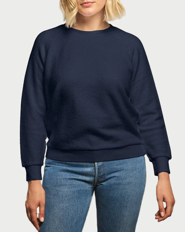 Woman wearing a navy blue sweatshirt and blue jeans against a beige background