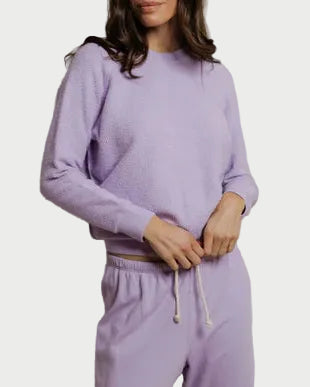 Woman wearing a purple sweater and pants against a plain background