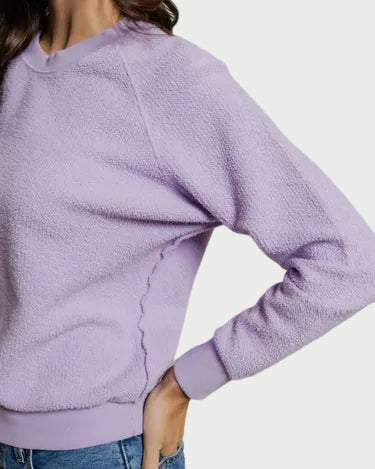 Person wearing a purple textured sweater and blue jeans on a plain background