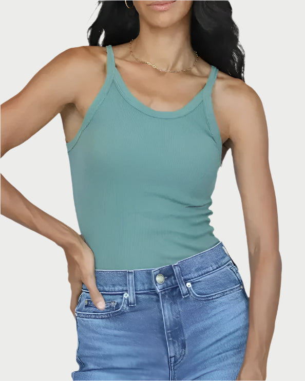 A person with long, wavy dark hair is wearing a green, form-fitting ribbed Annie Tank from perfectwhitetee and blue jeans. They are posing confidently with one hand on their hip against a plain background.